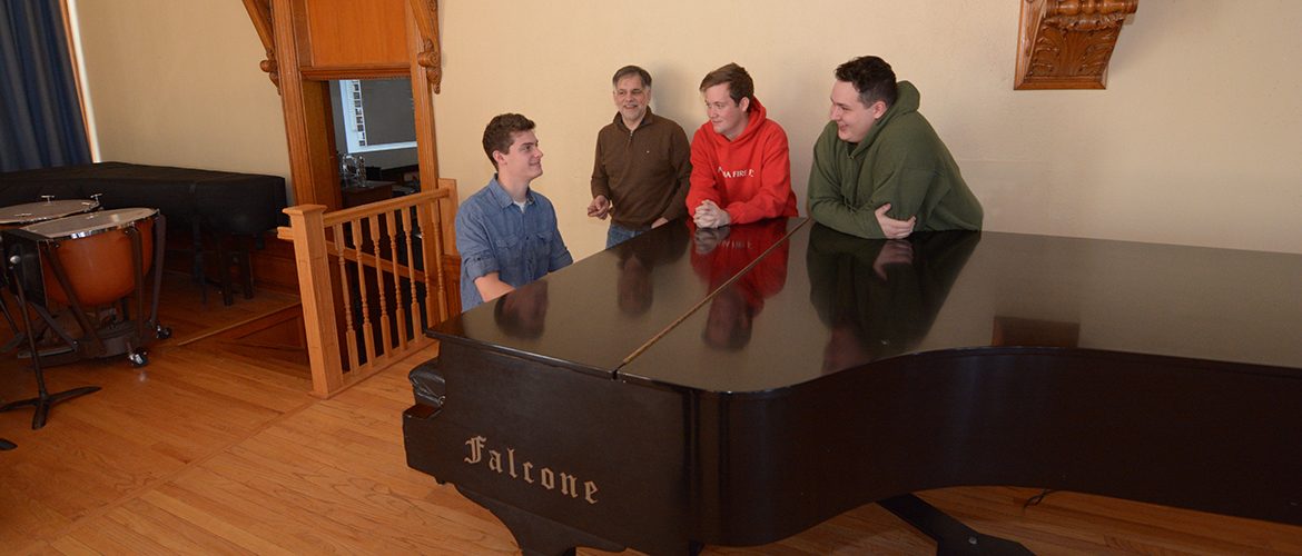 Professor with music students at a piano in Nordica auditorium performance hall